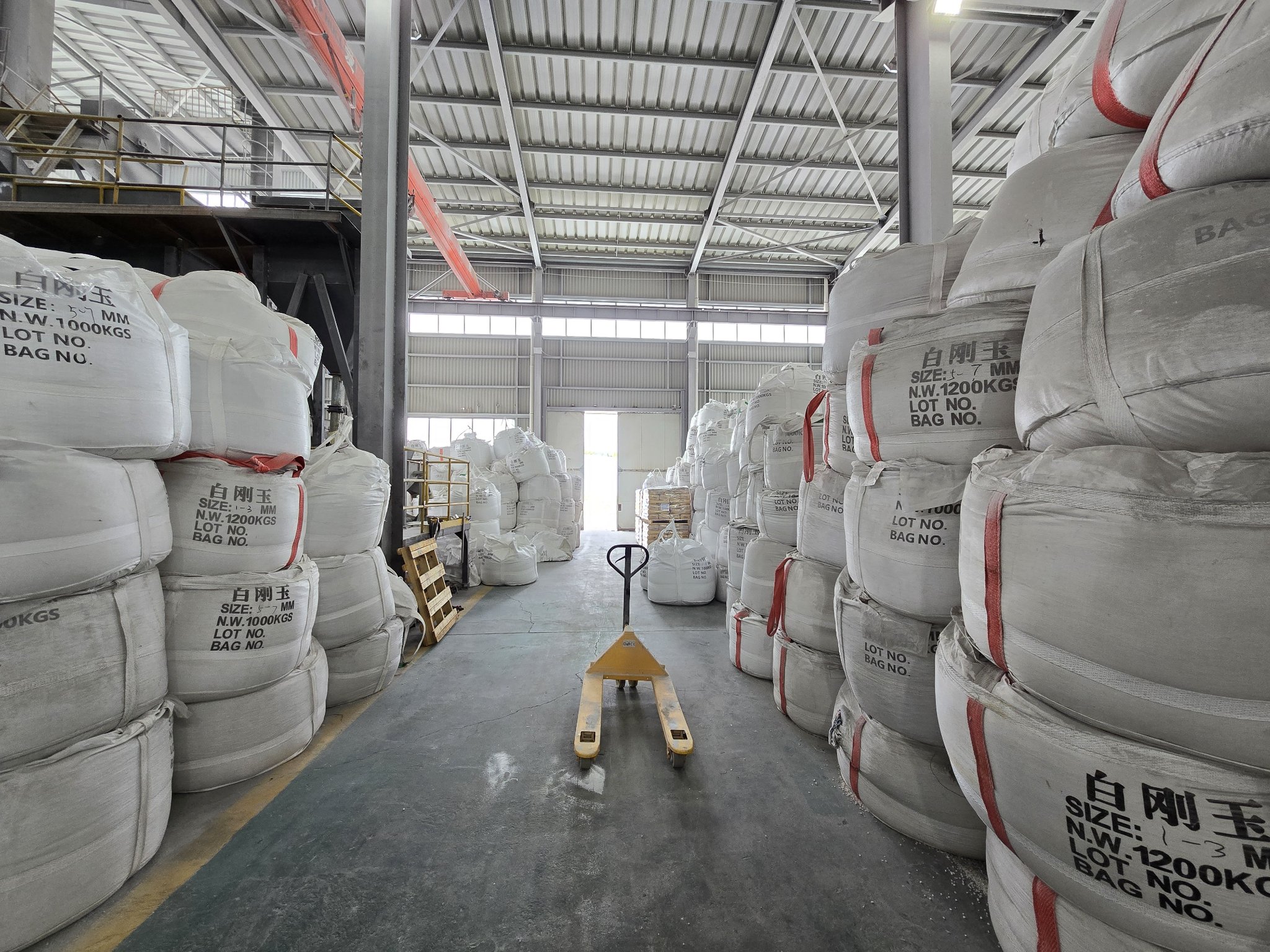 Warehouse aisle stacked with jumbo bags of white fused alumina